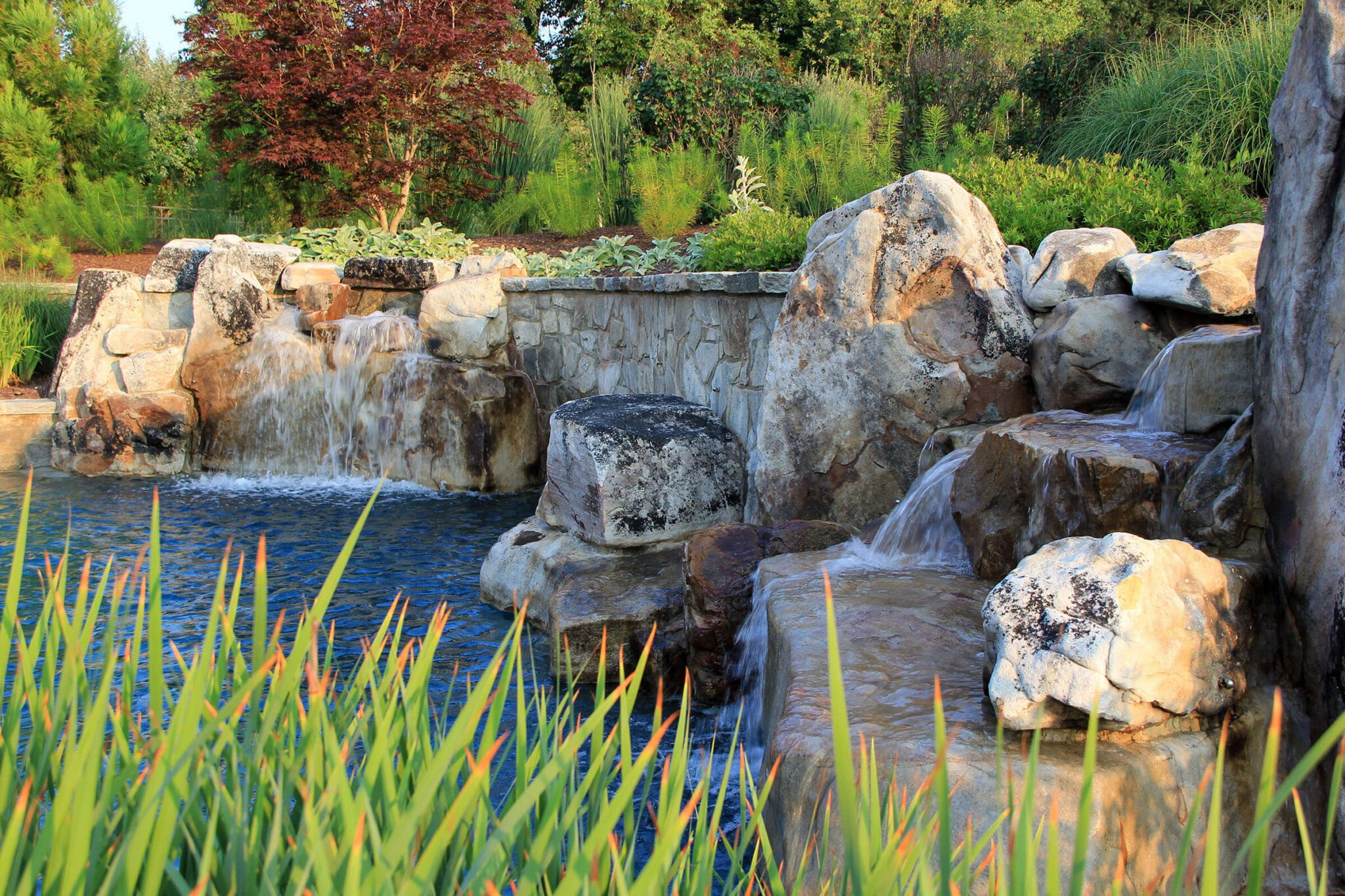 garden waterfall spills over boulders and retaining wal into a pool